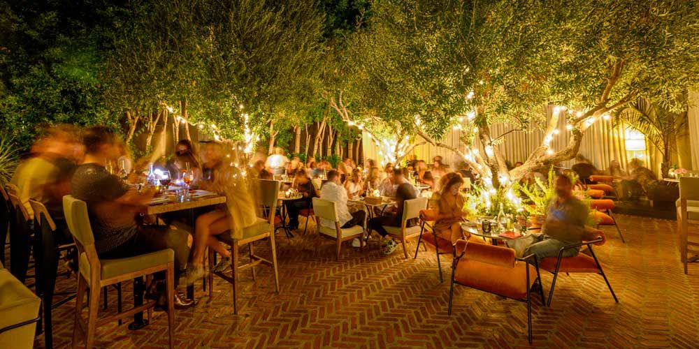 Laurel Hardware - A slightly unfocused shot of the crowded patio dining space with trees and hanging lights. 