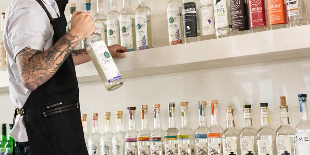 Gracias Madre - A tattooed barman selecting a bottle from a fully stocked bar in Hollywood.